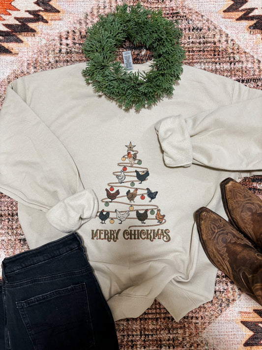 Flatlay of Merry Chickmas crewneck showing full chicken Christmas tree graphic with boots, garland, and denim styling
