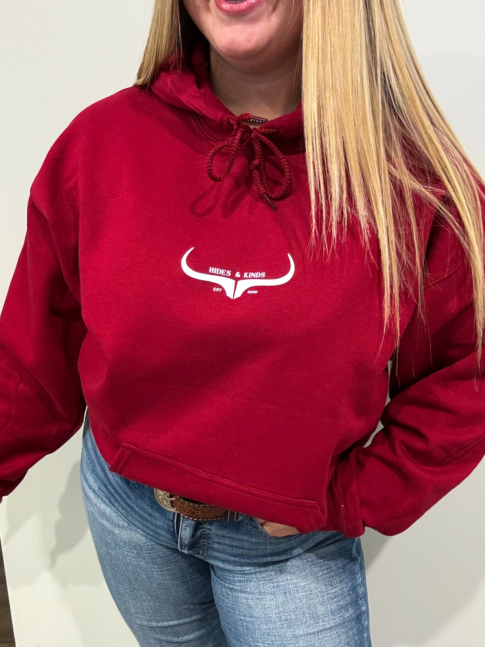 Woman wearing garnet red Hides & Kinds hoodie with original longhorn logo, side view