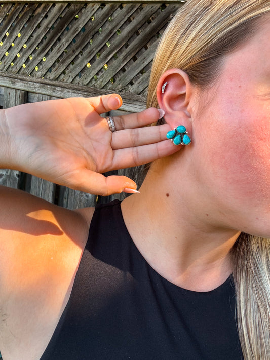 Close up of turquoise stud earrings styled on model with hand showcasing the size and detail