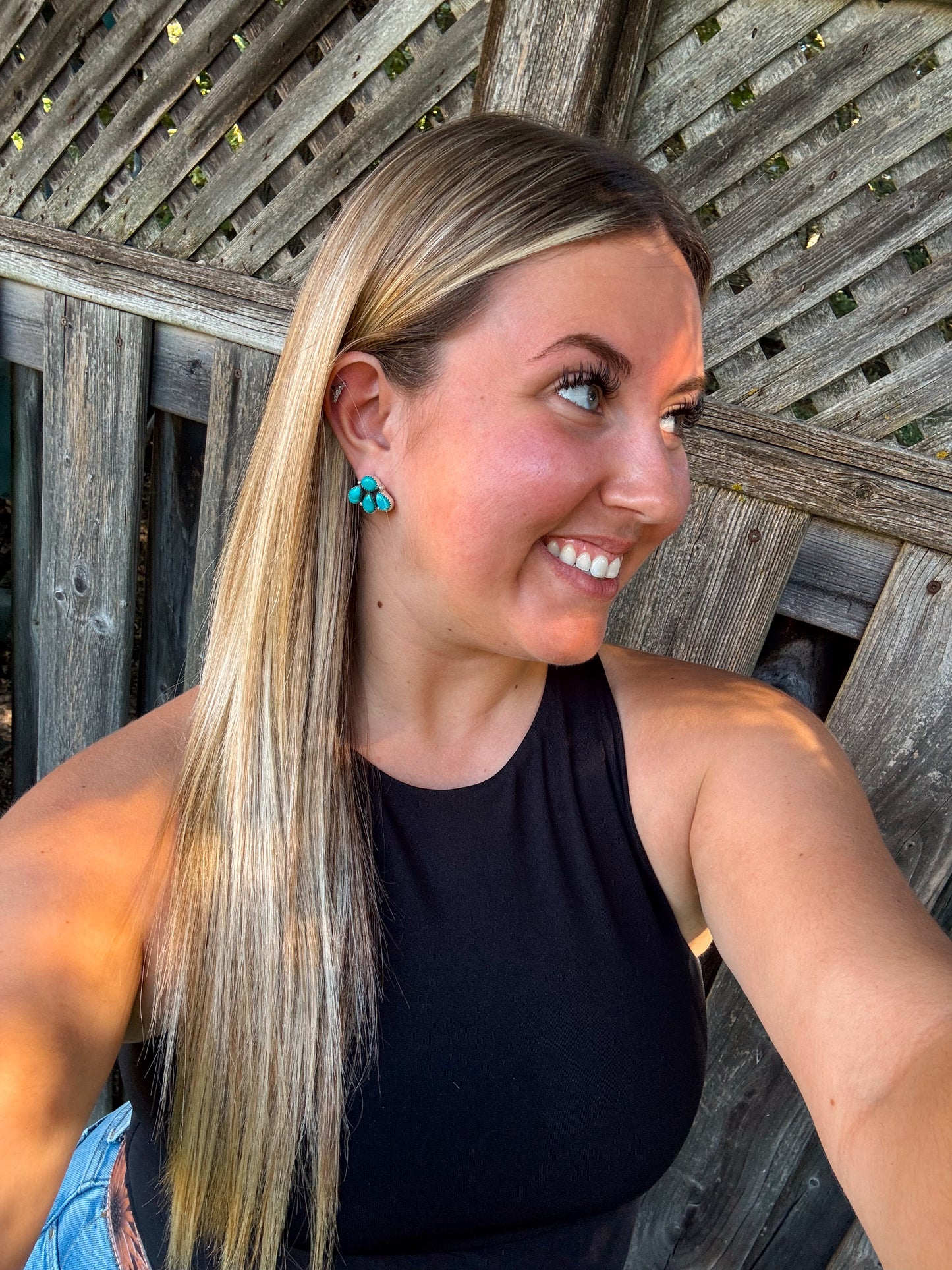 Smiling model wearing turquoise stud earrings with wooden fence background