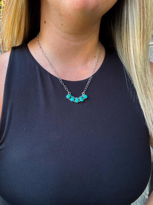 Close up of the Wild Sky Necklace featuring five turquoise stones set on a silver chain, worn with a black top.