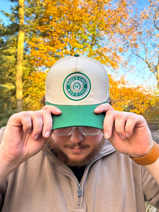 Front view of The Country Line Hat by Hides & Kinds in green and cream with circular Wild N Free patch logo.