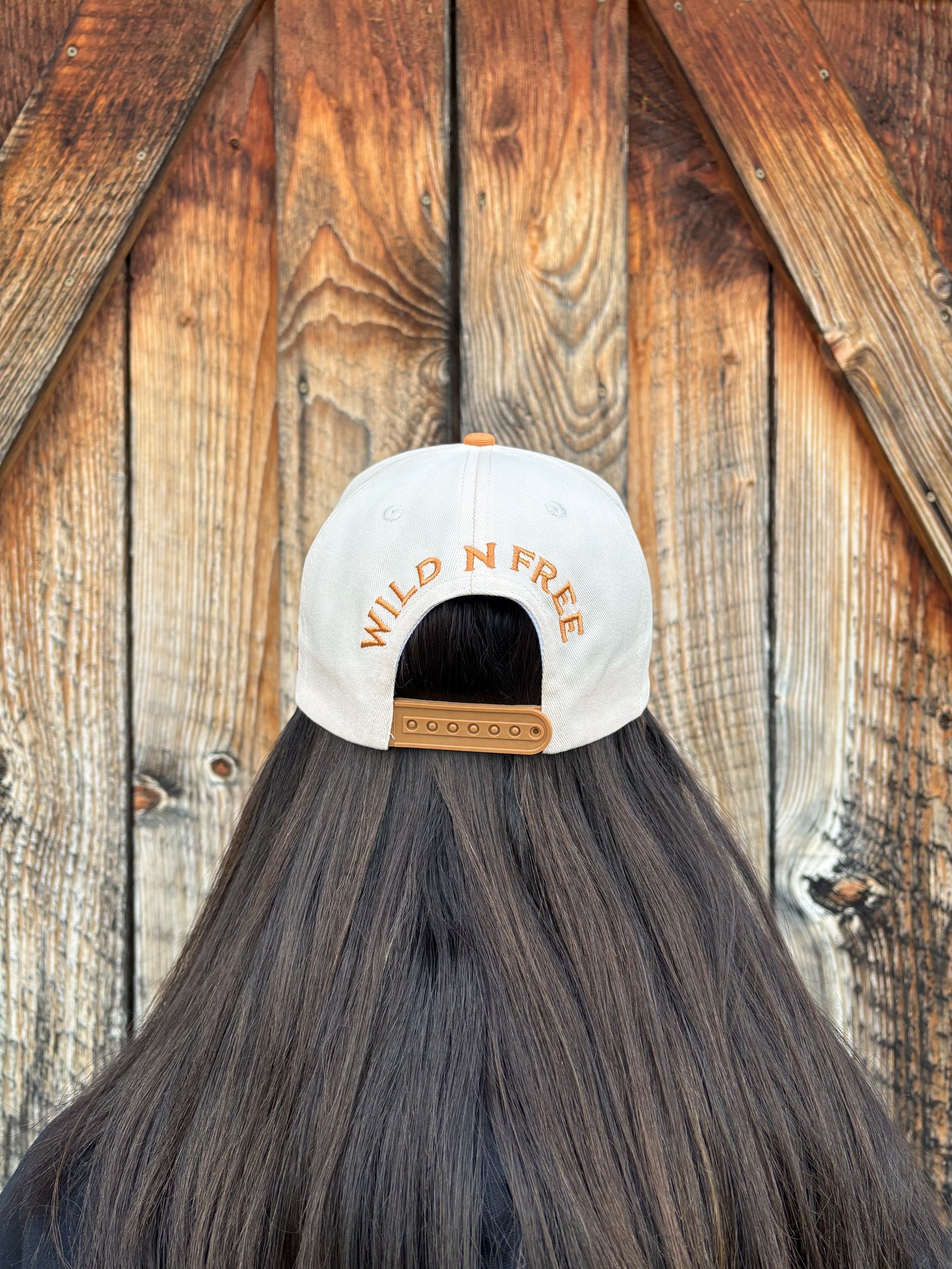 Back view of tan and cream Hides & Kinds Houston Hat showing Wild N Free embroidery and snapback closure.