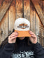 Front view of tan and cream Hides & Kinds Houston Hat styled on female model in front of rustic barn wall.
