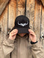 Front view of black and white Hides & Kinds Original Logo Hat styled on female model in front of rustic barn wall.