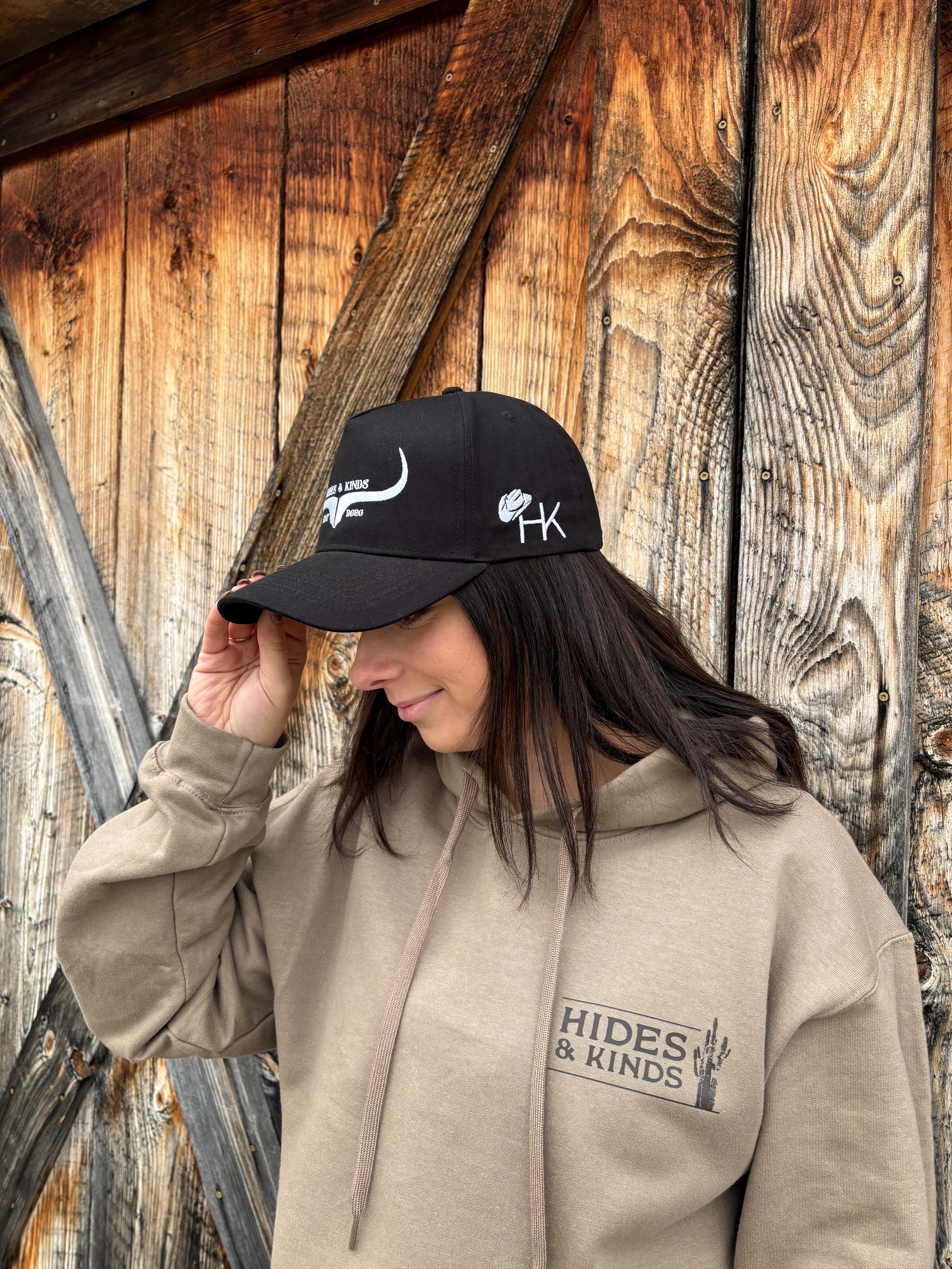 Side profile of Hides & Kinds Original Logo Hat in black and white with embroidered HK logo, styled on female model.