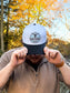 Front view of Hides & Kinds Stampede Snapback in teal and black styled on male model in outdoor fall setting.