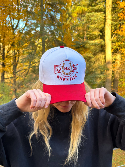 Angled front view of red and white Hides & Kinds Wild N Free Hat showcasing western horseshoe patch design.