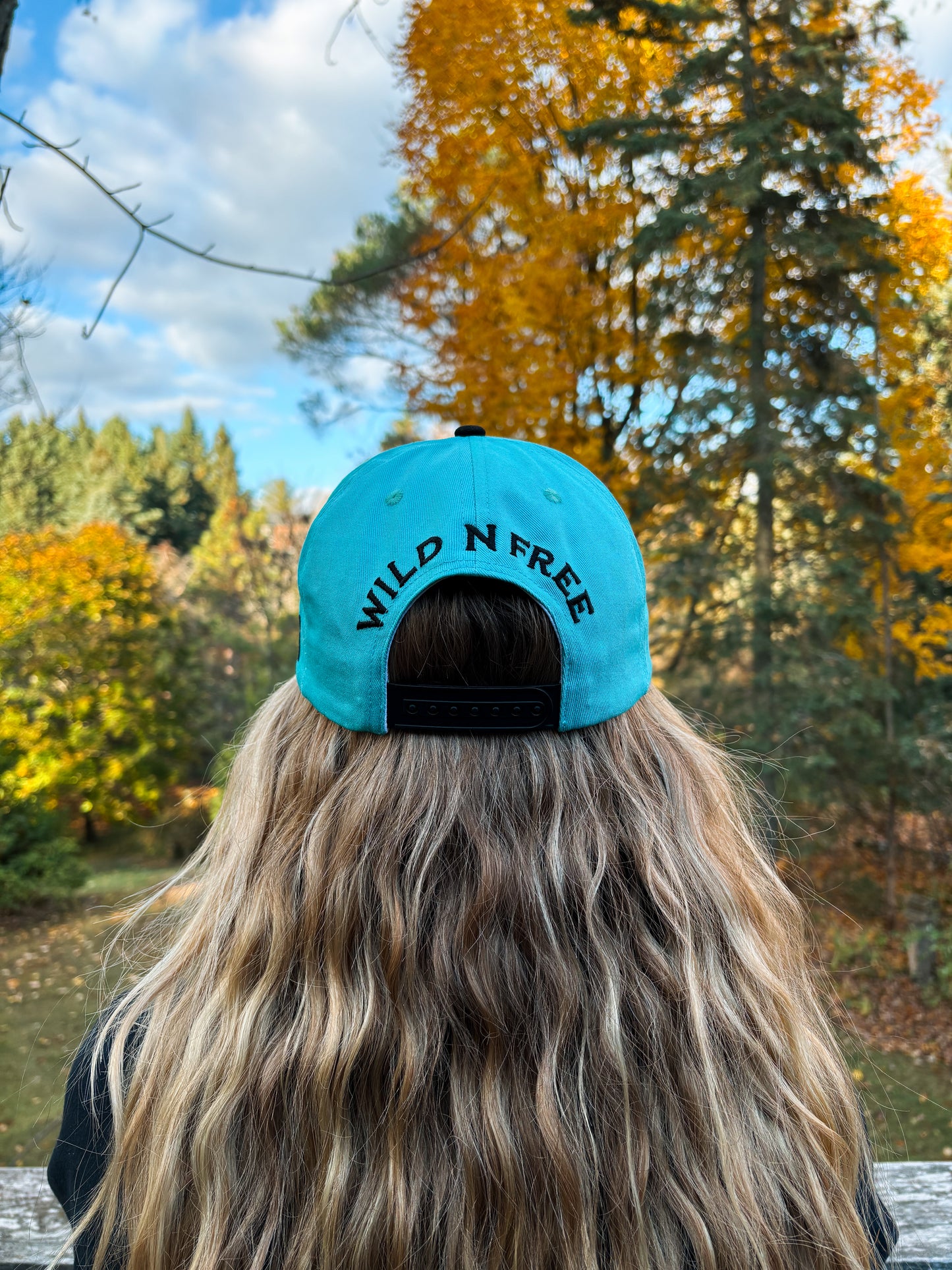 Back view of Hides & Kinds Wild N Free Hat in teal and black with embroidered Wild N Free lettering above the snapback closure.