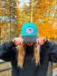 Front view of Hides & Kinds Wild N Free Hat in teal and black with signature logo patch.