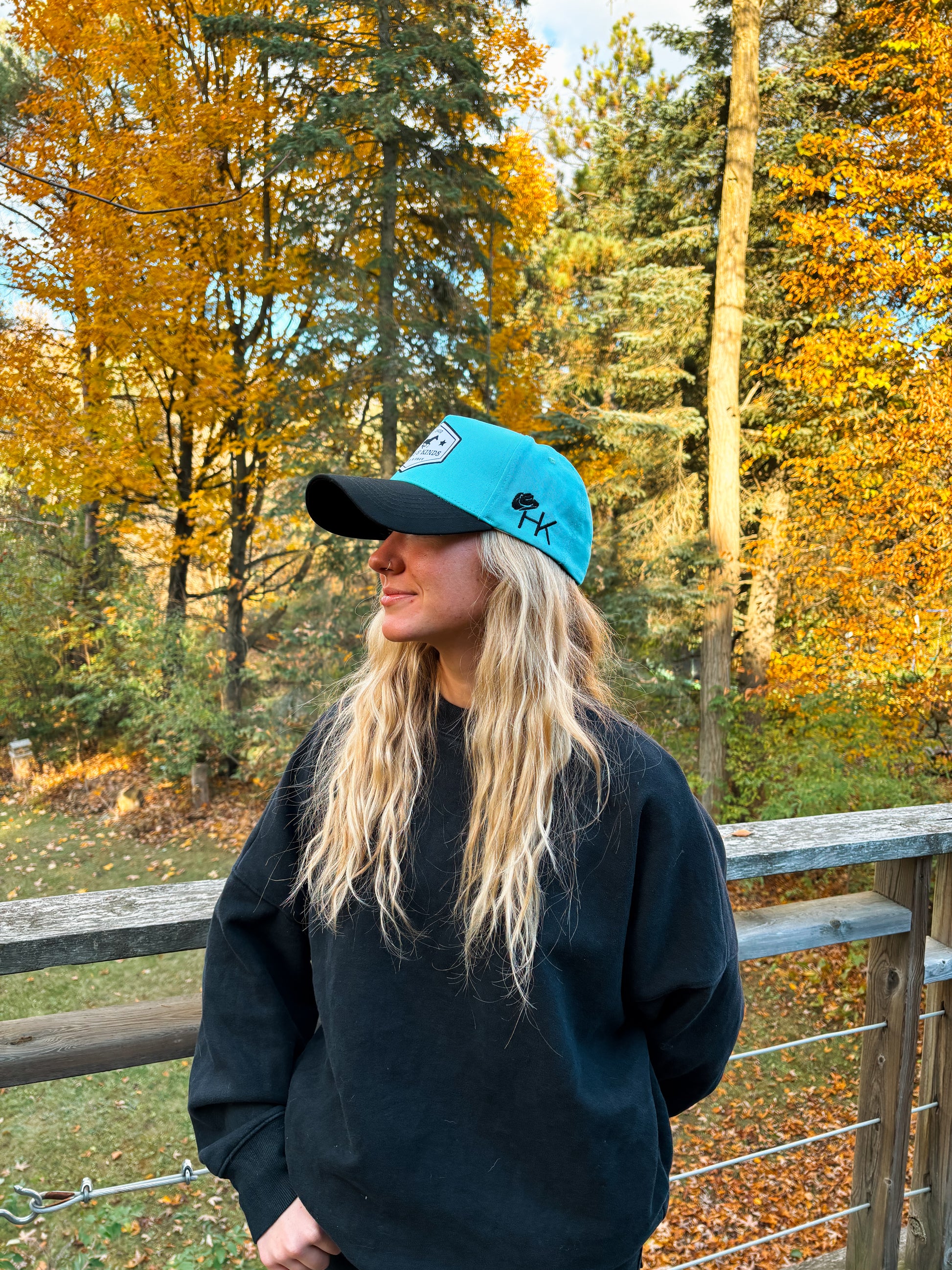 Side profile of Hides & Kinds Wild N Free Hat in teal and black with embroidered HK logo.