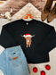 Western holiday sweatshirt with Highland cow design wearing Santa hat, styled with red ornaments and denim.