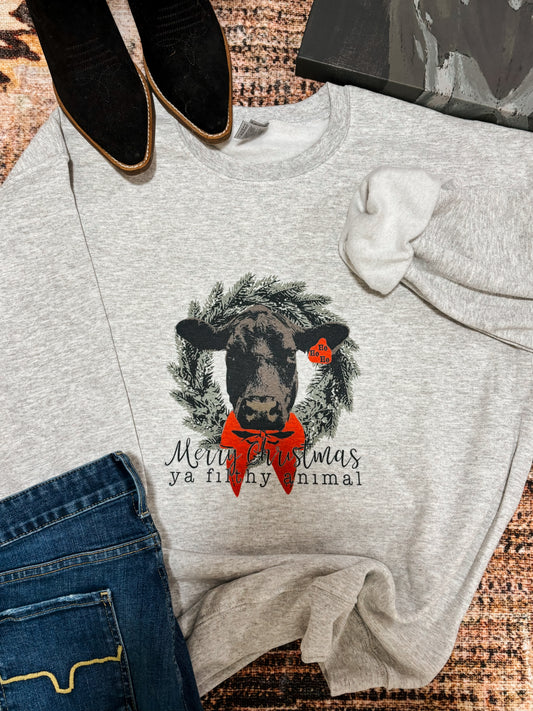 Flat lay of the Merry Christmas Ya Filthy Animal Crewneck with black suede boots and denim jeans, showcasing a festive cow graphic with a red bow and wreath