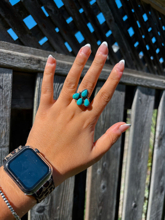 Close up of the Outpost Ring with five turquoise stones worn on the front of hand against wooden fence