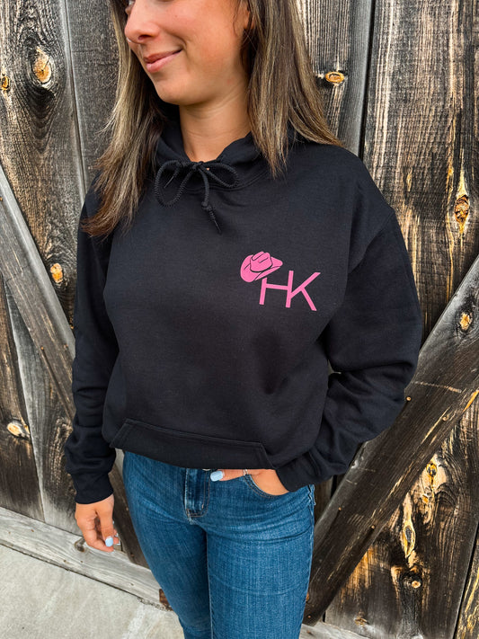 Close-up front view of black hoodie with pink HK cowboy hat logo