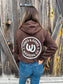 Model wearing chocolate brown Outrider Hoodie with oversized Hides and Kinds horseshoe logo on back.