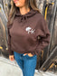 Close-up of HK cowboy hat logo on chocolate brown Outrider Hoodie.