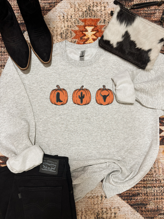 Pumpkin Patchin’ crewneck with three orange pumpkins featuring a boot, cactus, and longhorn design, styled with black denim, cowhide purse, and western boots