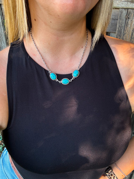 Close up of the Three Rivers Necklace featuring three oval turquoise stones set in silver, worn on a model with a black tank top.