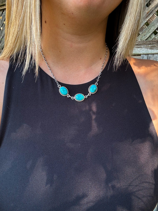 Three Rivers Necklace shown from a side angle, highlighting the silver chain and vivid turquoise stones against a black top.