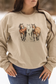 Model wearing the Trail Trio Crewneck standing in the snow with three galloping horses printed on the front, featuring a neutral sand colored sweatshirt perfect for cozy western style lovers.