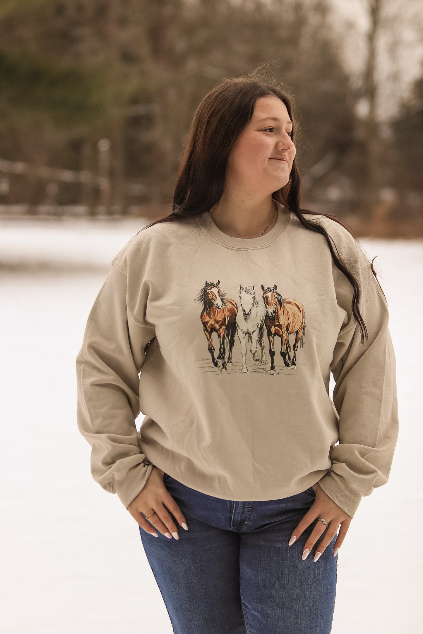 Trail Trio Crewneck styled outdoors in a snowy, natural setting with a trio of illustrated horses on the chest.