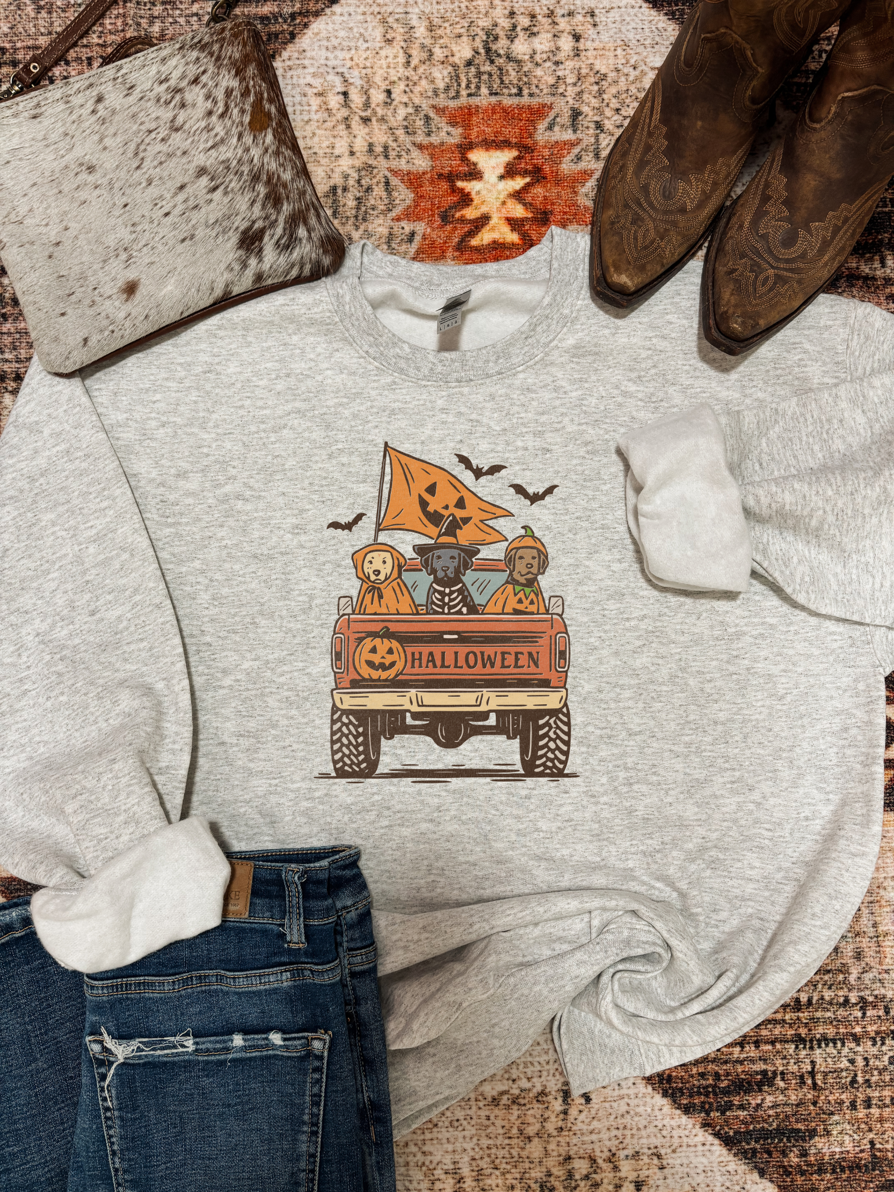 Trick or Truck crewneck with cartoon dogs in the back of a Halloween pickup truck, styled with jeans, cowhide purse, and cowboy boots