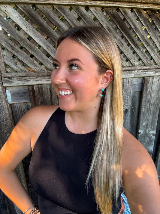 Model smiling while wearing Turquoise Canyon Dangle Earrings with sunlit wooden fence backdrop.
