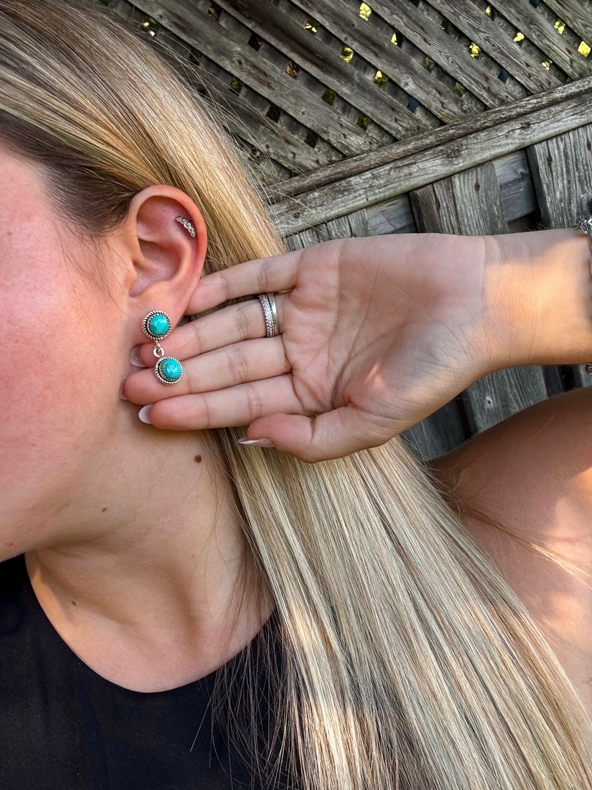 Hand holding turquoise dangle earrings with rustic silver frame, styled against long blonde hair.