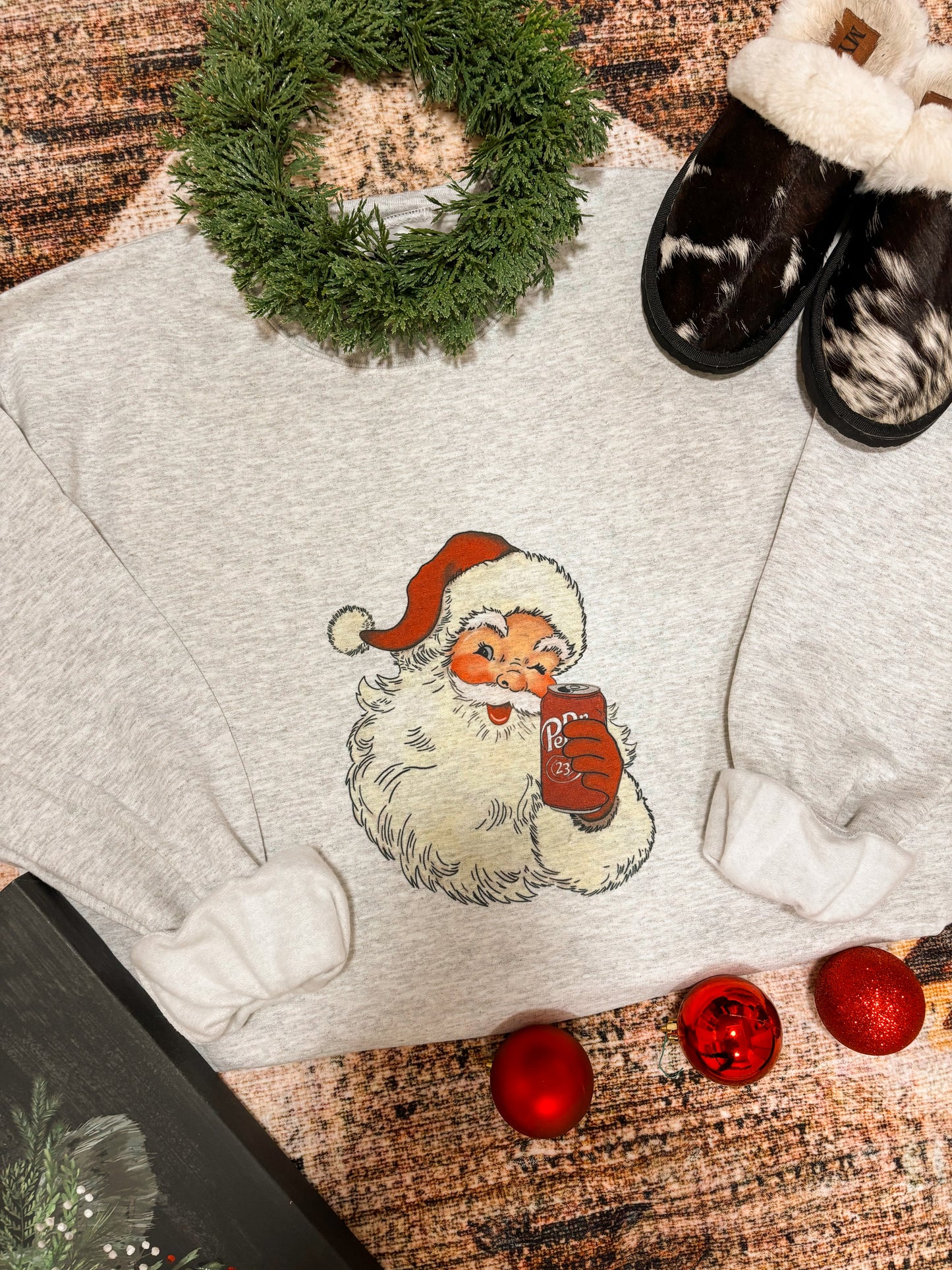 Grey crewneck sweatshirt with vintage Santa print, surrounded by a faux wreath and holiday slippers.