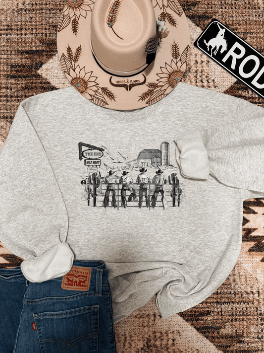 Heather grey crewneck with vintage style Wild West cowboy graphic, styled with denim, beige sunflower hat, and rodeo sign