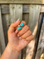 Adjustable turquoise ring with two genuine stones shown outdoors with wood background.