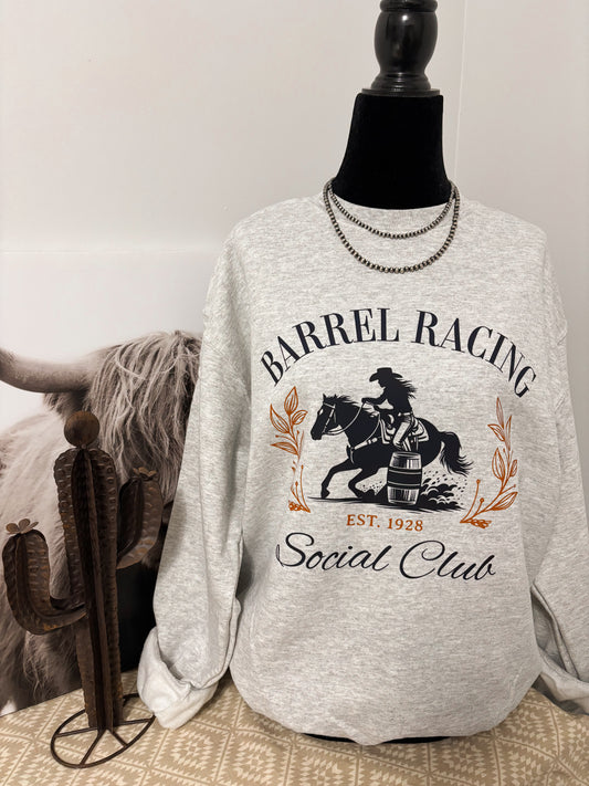 Western inspired grey crewneck with bold barrel racing design, styled beside a decorative cactus and rustic décor.