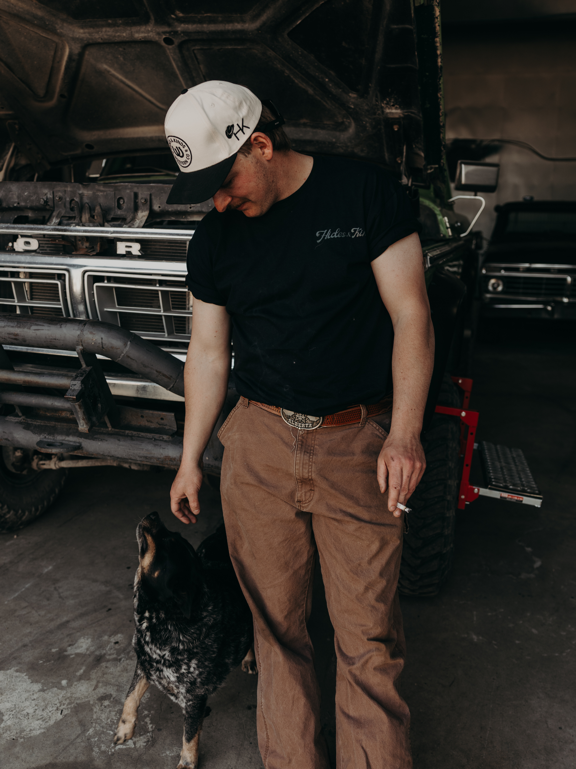 Model wearing the Hides & Kinds Big Buck Tee with a cattle dog, showcasing the men's country lifestyle graphic tee.