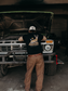 Model wearing the Hides & Kinds Big Buck Tee featuring a deer graphic while standing in front of a vintage truck.