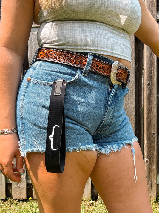 Black wristlet strap with white HK longhorn bracket logo, western keychain accessory styled with denim and silver buckle belt.