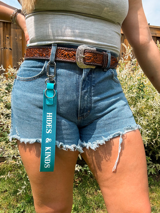 Blue branded wristlet strap with “Hides & Kinds” print – attached to belt loop for a bold, everyday western look.