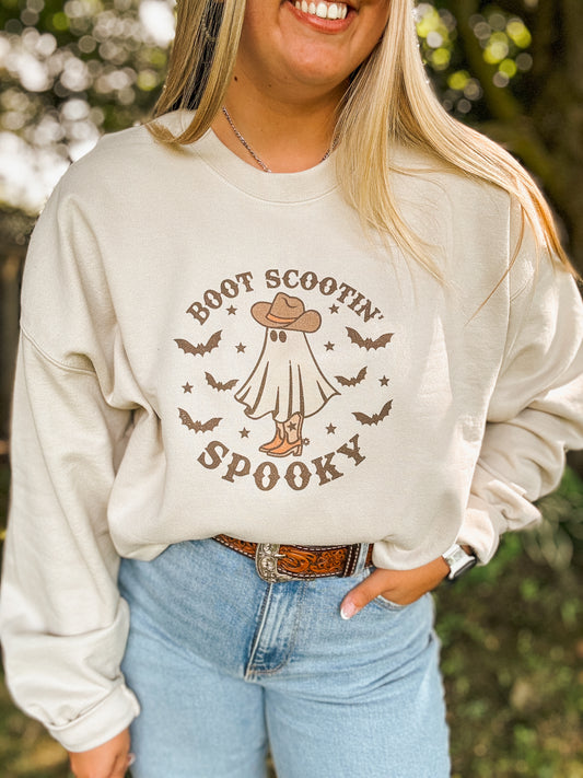 Woman wearing Boot Scootin' Spooky crewneck with ghost and cowboy hat design, styled with denim and western belt.