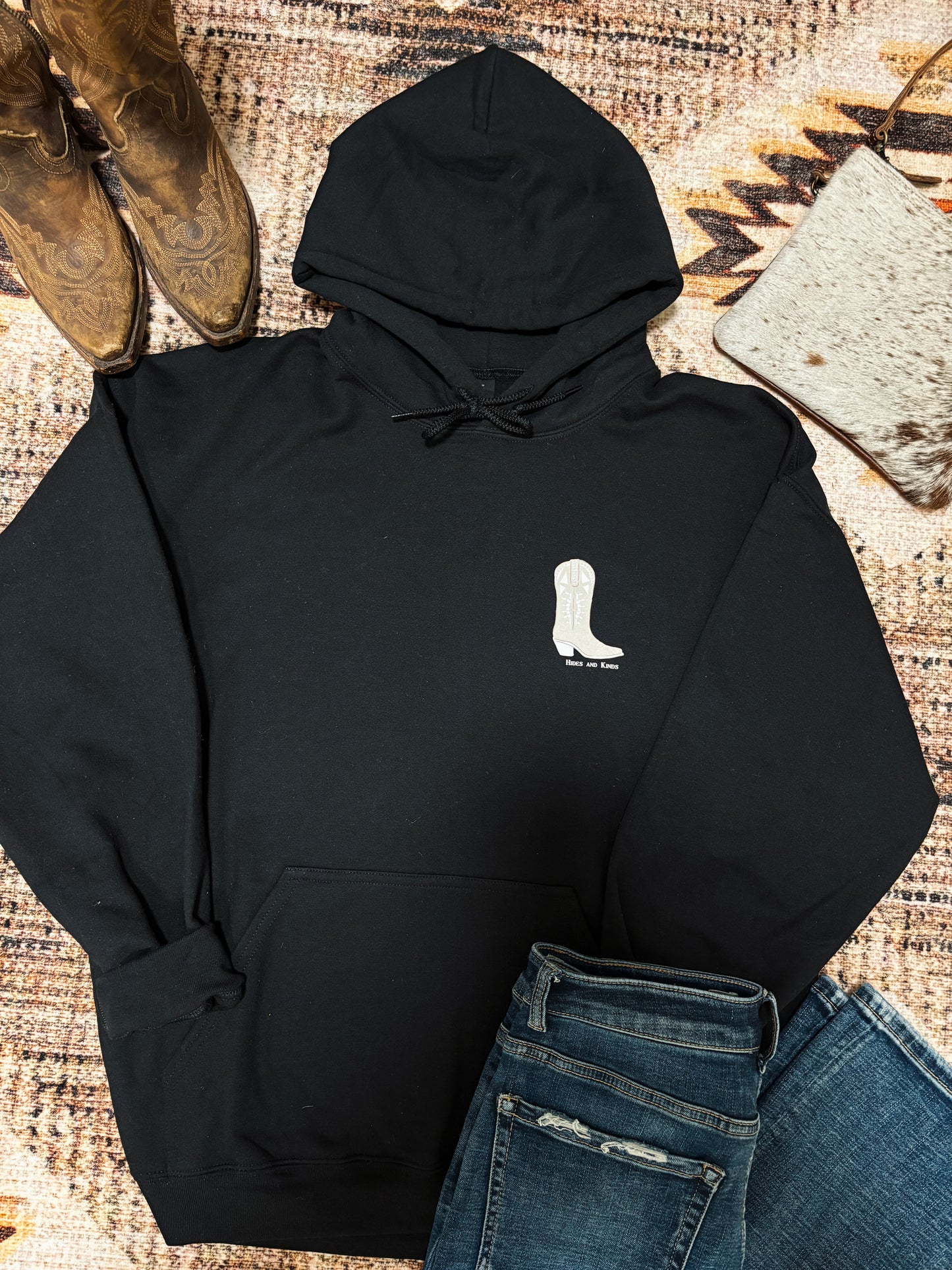 Front view of black Hides and Kinds hoodie with small white cowboy boot logo on the chest