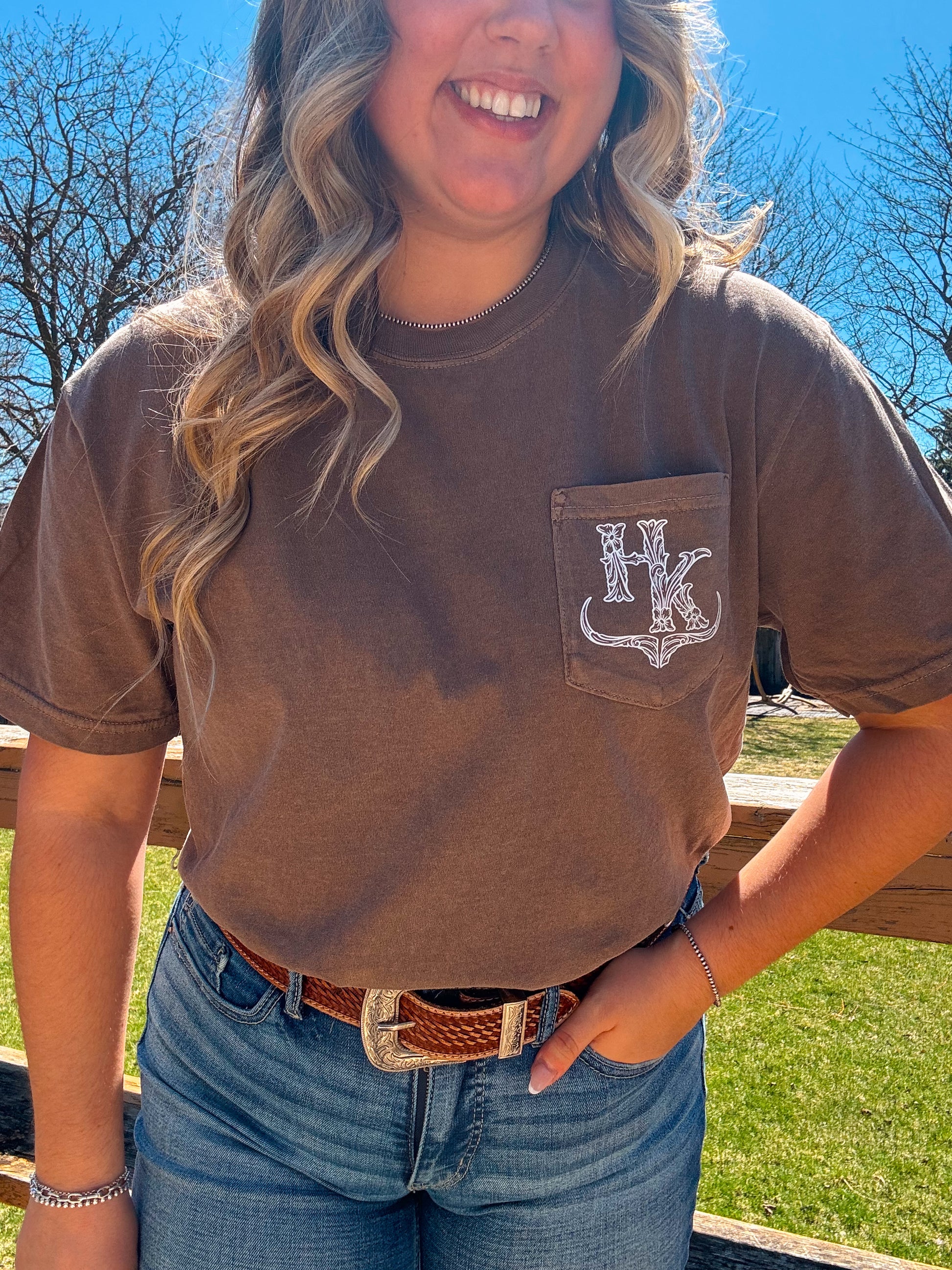 HK Branded Pocket Tee in espresso brown photographed outdoors in natural light, showcasing the pocket and logo detail.