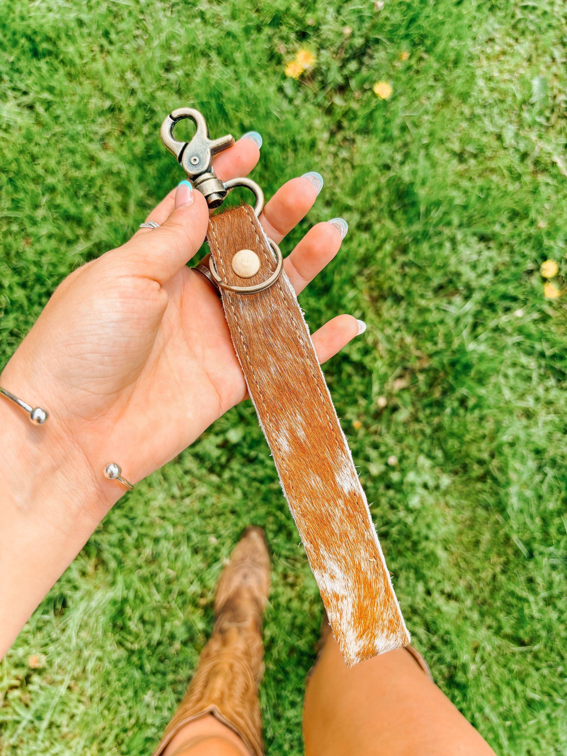 Western cowhide wristlet keychain accessory held by woman in cowboy boots – Hides & Kinds