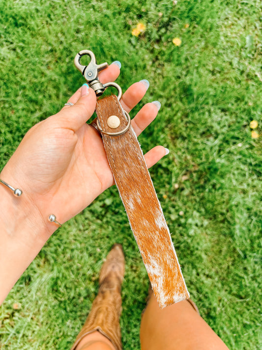Western cowhide wristlet keychain accessory held by woman in cowboy boots – Hides & Kinds