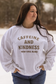 Close up of a white crewneck that says "Caffeine and Kindness Brew-tiful Blend" from Hides & Kinds, styled for winter.