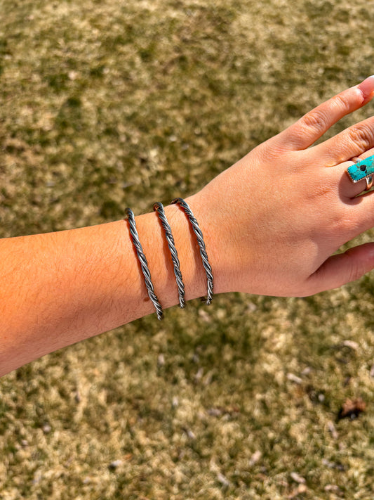 Double twisted rope cuff bracelet in sterling silver shown on wrist outdoors