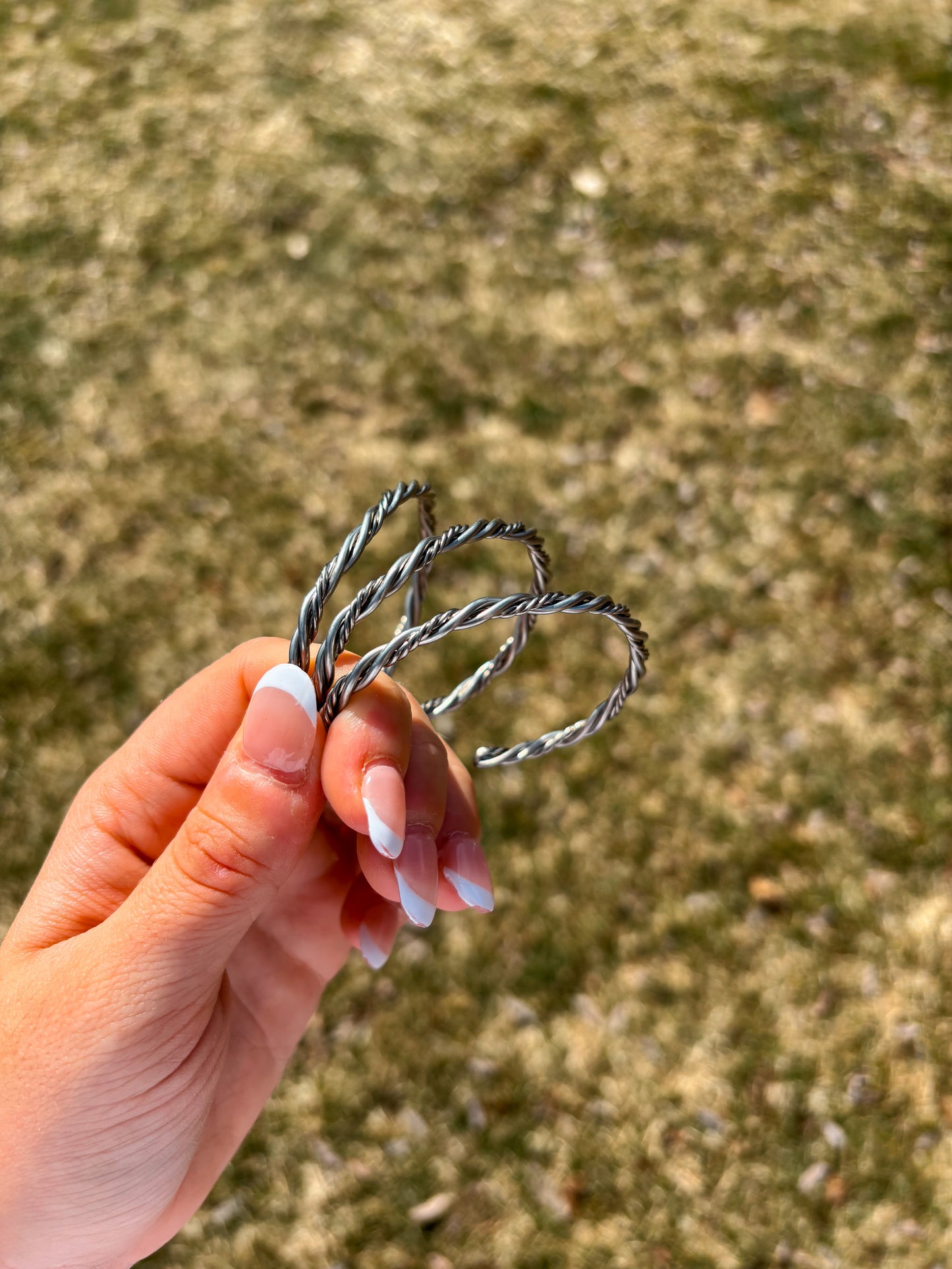Hand holding sterling silver double twisted rope cuff bracelet against natural background