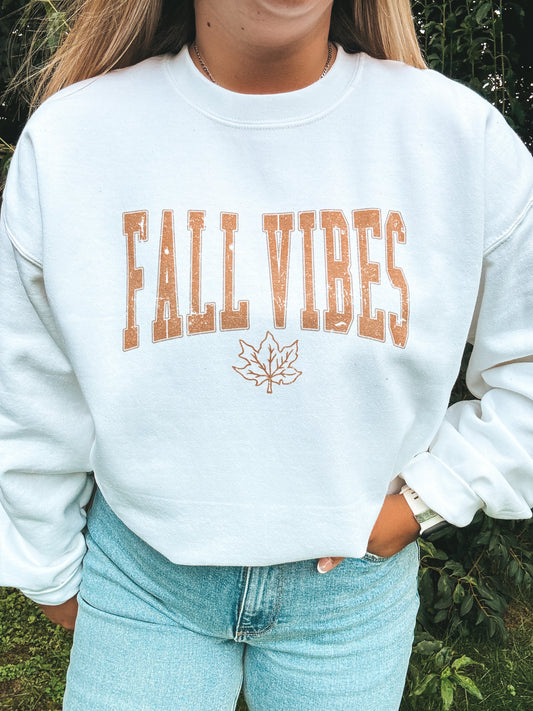 Woman wearing Fall Vibes crewneck in white with rust text, styled with light wash jeans.