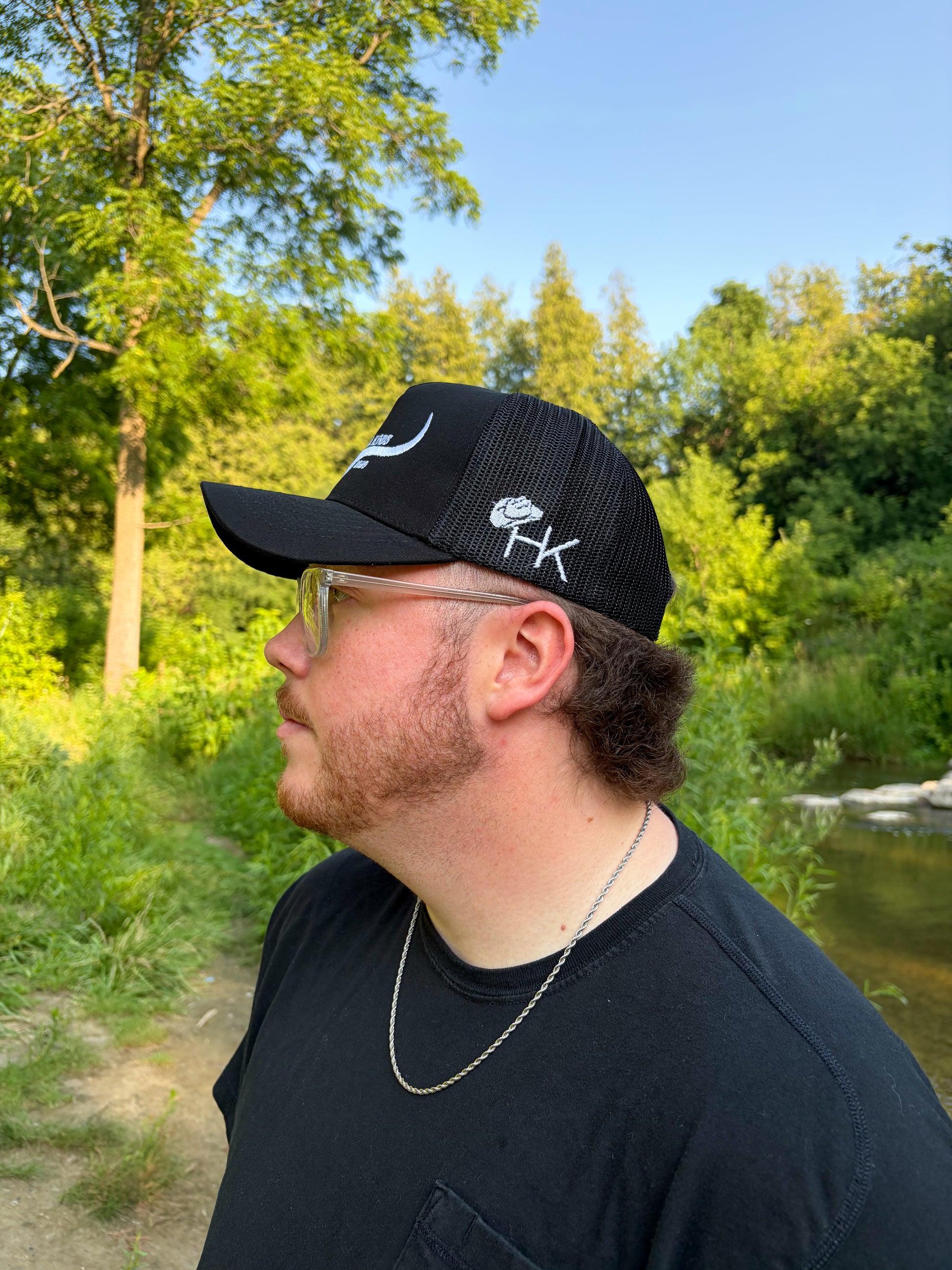 Side view of black Hides & Kinds meshback hat with white embroidered HK cowboy hat logo