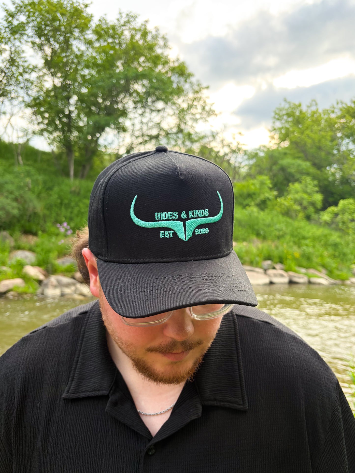 Black Hides & Kinds western hat with teal embroidered longhorn logo shown from the front