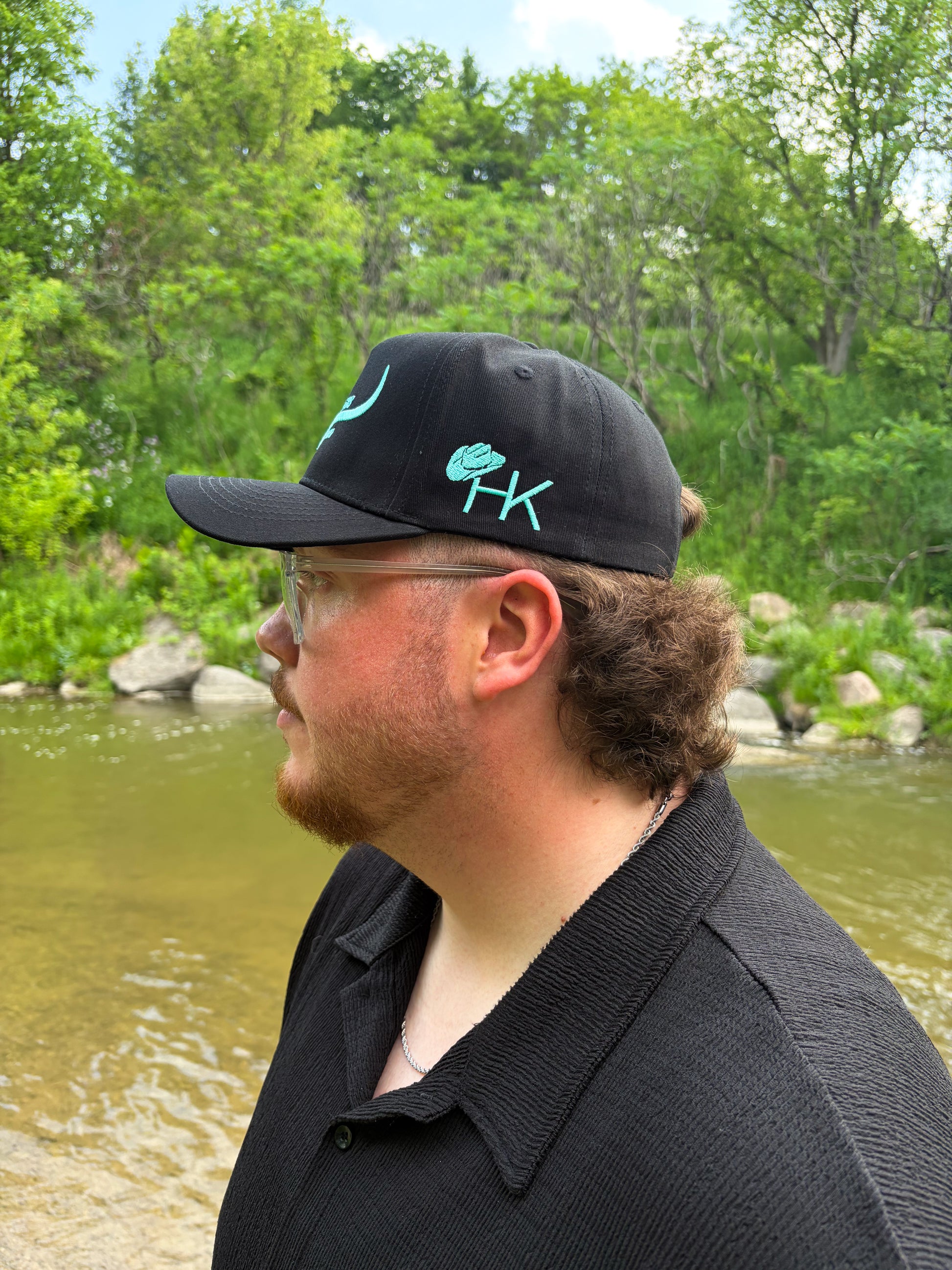 Side view of the Hides & Kinds black and teal hat featuring embroidered HK cowboy hat logo