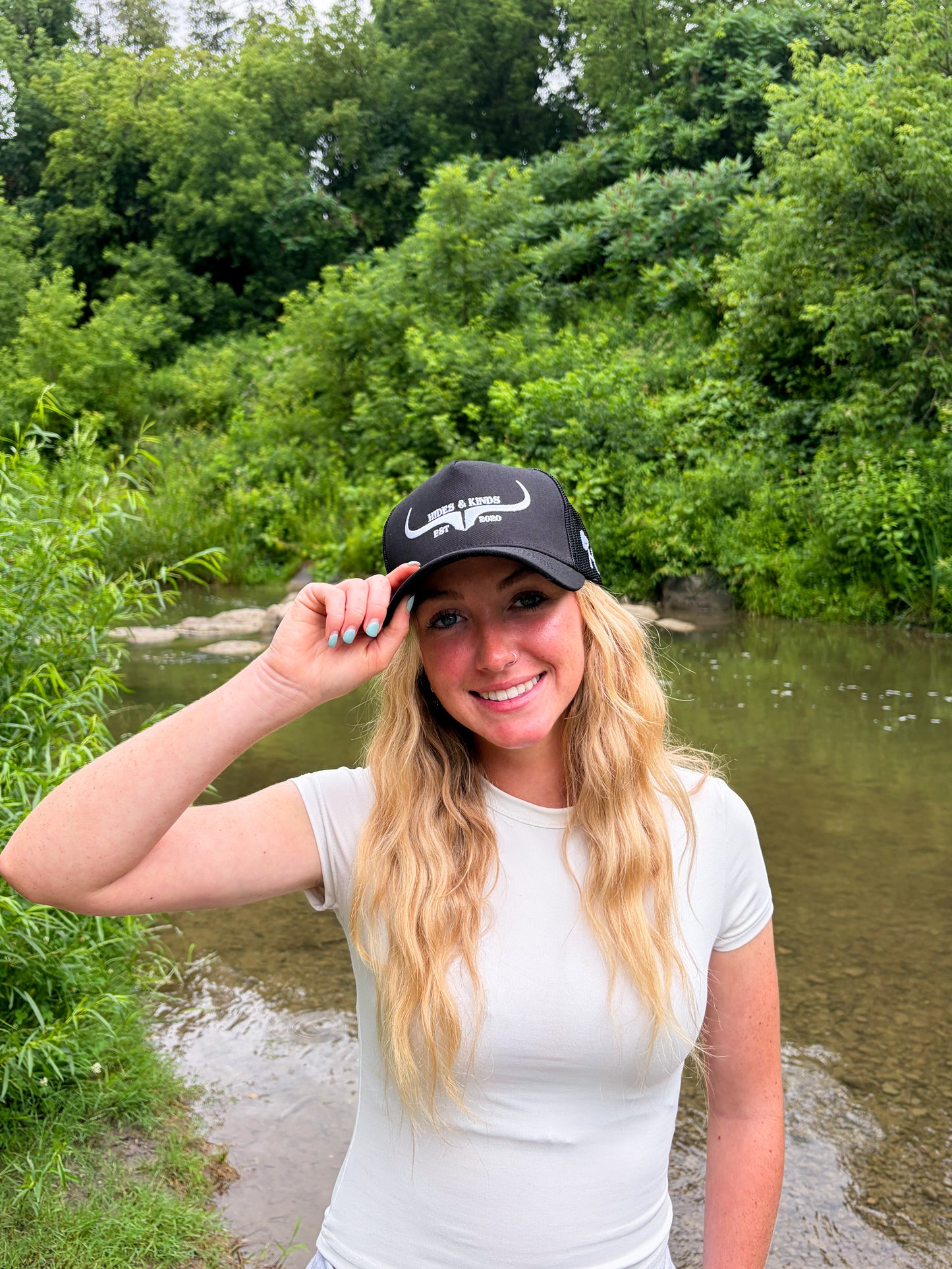 Woman wearing the Hides & Kinds Original Logo black and white meshback trucker hat